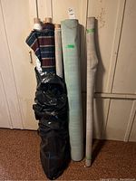 Photo showing seven rolled fabrics and vinyls standing upright against a wall with visible textured, striped, solid and floral patterns