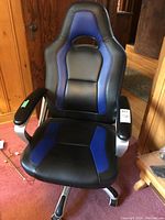 Front view of the black and blue gaming chair showing the racing-style seat with padded armrests and caster wheels.