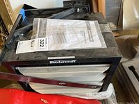 Top and front view of a black Mastercraft garage heater with mounting brackets and an instruction manual on top.