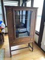 Wooden hutch cabinet with glass door and decorative inlays, showing front view standing upright.