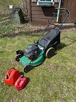 View of the green Craftsman gas lawnmower on grass with two red Jerry cans in front.