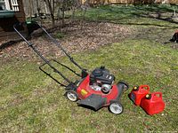 Yard Machines 140cc gas lawn mower and two red 5L jerry cans displayed outside on grass with leaves around.