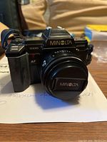 Front view of Minolta Maxxum 7000 camera body with attached lens and front lens cap showing brand and model