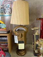Full view of the parking meter lamp showing gold-colored meter base with beige pleated shade, placed next to trophies and books.