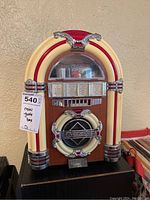 Full view of the mini jukebox style radio showing cream and red plastic accents and wood finish with tag