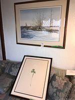 Two framed prints displayed on a floral patterned sofa and wall: a winter landscape photo and an embossed rose print.