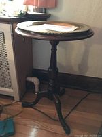 Side view of the small round pedestal table showing the three curved legs and turned central pedestal.