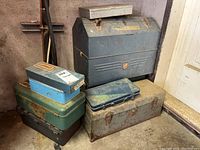 Seven assorted metal and plastic toolboxes stacked together showing variety of sizes and colors, weathered condition.