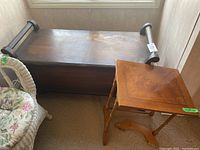 Photo showing wood cedar chest with scroll handles and wooden side table beside it