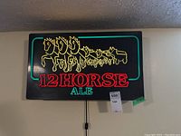 Front view of black rectangular illuminated sign with 12 yellow outlined horses and red-green '12 HORSE ALE' text in neon style.