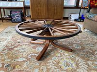 Angle view of wooden wagon wheel coffee table showing wood spokes, round rim and four-legged base on carpet.