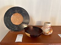 Set of three items arranged on a wooden surface: wooden plate, wooden bowl, and ceramic vase.
