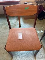 Front view of the chair showing curved wooden backrest and rust fabric upholstered seat with label.