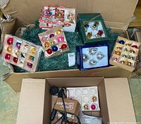 Box with multiple sets of Christmas glass ornaments in original boxes and loose in box along with extension cord and plastic packing material