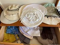 First photo shows several light-colored bucket hats and a pair of gloves inside a drawer including knit gloves and a brown pair beside folded hats.