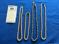 All four pearl style beaded necklaces laid out on blue fabric background.