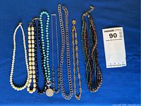 Full view of all seven necklaces laid flat on blue surface showing length and variety of bead types and chains.