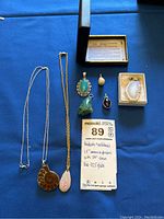 Overview of pendants and necklaces displayed on blue cloth including ammonite fossil, agate, turquoise, pearl, geode charms, and silver chains.