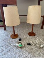 Pair of teak table lamps side by side on carpeted floor showing full lamps and shades.