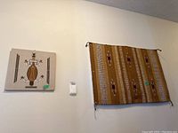 Wide view showing the Native American sand art plaque on left and the woven tapestry on right hanging on the wall.