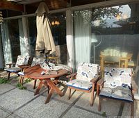 Wide shot of 4 wooden chairs with cushions around round table and umbrella on concrete patio
