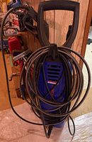 Front view of blue Simoniz S1650 pressure washer with cord wrapped around it, visible handle and hose attachment point.