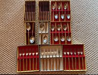 Overview photo showing all sets including forks, tablespoons, teaspoons, and cutting tools in their original boxes with red felt lining arranged on the floor.