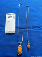Two necklaces shown side by side on a blue background, one with amber pendant and one with coral and turquoise pendant. Note indicating '925' sterling silver.