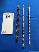 Three sterling silver bracelets laid out on blue background with measuring card showing length details.