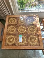 Full top view of the square tile top table showing the 3x3 pattern of decorative tiles with brown and yellow starburst designs within a light wood frame.