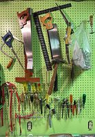 Wide shot of various hand tools hung on pegboard including saws, screwdrivers, hammer, ruler and hooks