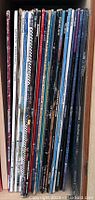A side view of 18 vinyl records with spines showing artist names and album titles in sleeves, mostly from the 70s and 80s.