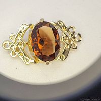 Close-up clear views of the gold-tone Celtic brooch with large oval faceted cairngorm stone showing Celtic knot designs and color.