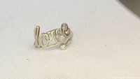 Clear photograph of the Alex and Ani silver ring with 'love' script design on a neutral background.