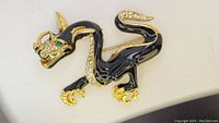Front view of black enamel dragon brooch with rhinestones and green eye on neutral background