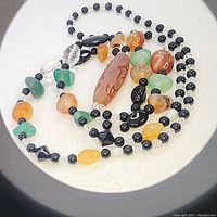 Photo showing the full necklace with distinctive beads including the elongated reddish Dzi bead, green chrysoprase, citrine, black and clear beads.