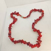 Photo of a vintage coral chip necklace laid flat on a white surface showing the full length and details of irregular red coral chips and metal clasp.