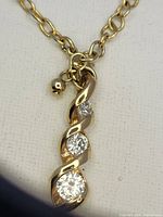 Close-up of the pendant showing the three round clear stones set in a twisting gold metal frame along with part of the gold chain and a small bead accent near the pendant.