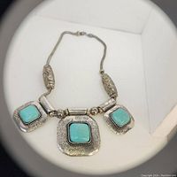 Full view of the antique handmade necklace with three turquoise stones and silver swirl patterned metal.