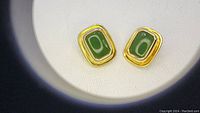 Close-up of green nephrite clip earrings showing rectangular stones with smooth polished surfaces, bezel-set in gold-tone metal frames.