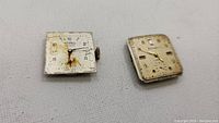 Two square vintage watch movements showing front dials and winding crowns placed on white surface. Left movement on Tissot dial, right on unbranded dial.