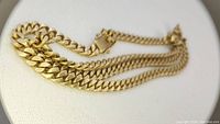 Coiled gold-tone Cuban link chain on white display