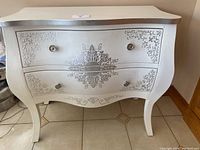 Front view of the white accent table with silver floral motifs and two drawers.