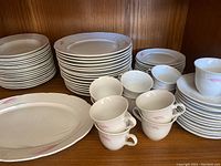 Overview of stacks of dinner plates, side plates, cups, saucers, and platter with pink tulip floral pattern and basket weave edge texture