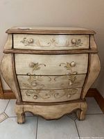 Front view of a 4-drawer chest with floral painted design, distressed cream finish and curved sides.