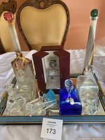 Full view of crystal barware set including various decorative decanters and stoppers arranged on mirrored tray.