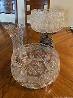 View of crystal vase, smaller crystal bowl on metal stand, and larger crystal bowl on wooden table
