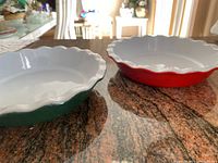 Two ceramic pie plates with fluted edges; one red and one green exterior with white interior.