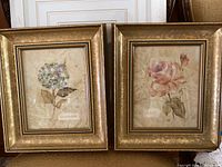 Two framed floral prints side by side, one hydrangea and one rose with gold frames.