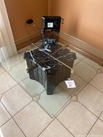 Square glass top table with black marble-look base and metal support frame.
